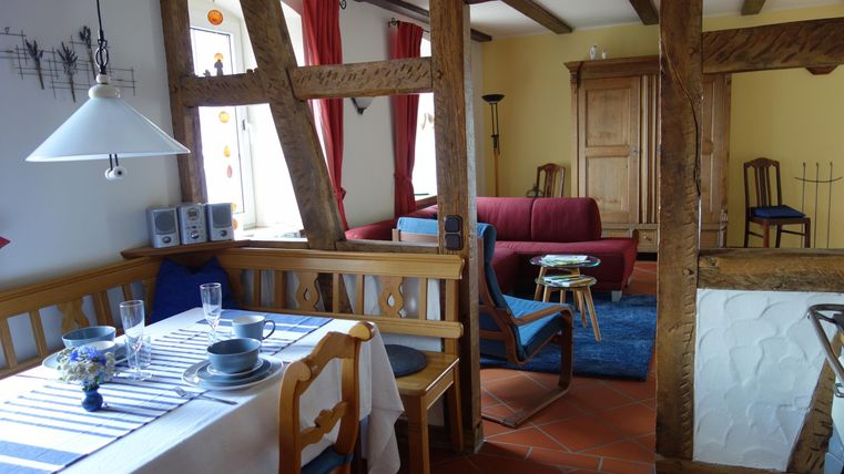 Een gezellige woonkeuken met een eettafel en stoelen. Op de achtergrond zijn een rode bank en een blauw tapijt te zien.