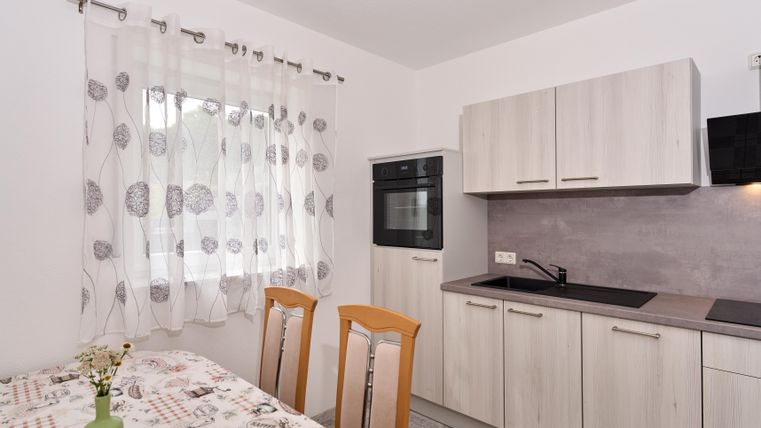 Eine moderne und helle Küche mit Holzschränken und einem Essbereich. Das Fenster ist mit einem leichten Vorhang dekoriert und der Tisch hat eine hübsche Tischdecke.