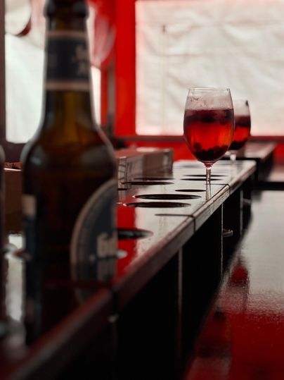 Ein Tisch mit einem Bier und einem Glas rotem Getränk. Im Hintergrund sind weitere Gläser sichtbar.