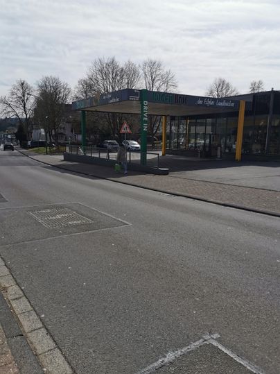 Eine moderne Tankstelle an einer Straße. Im Hintergrund sind Bäume und ein klarer Himmel zu sehen.
