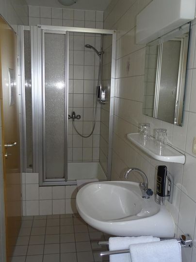 Ein einfaches Badezimmer mit einer Dusche, einem Waschbecken und einem Handtuchhalter. Die Wände sind gefliest und die Einrichtung ist praktisch.