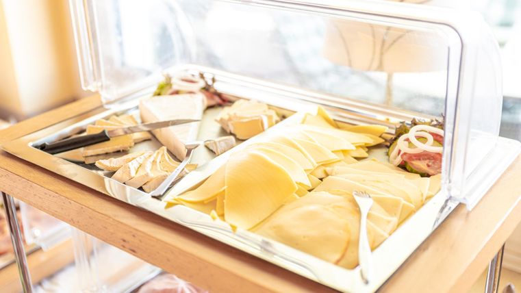 A buffet with various types of cheese and sausage. The artistically arranged products are presented under a glass cover.