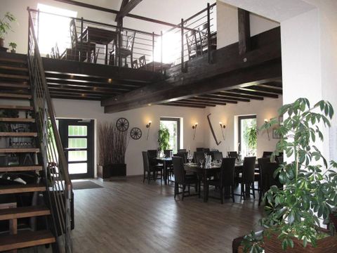 Moderne Scheune mit Holzbalken, Treppe, Esstischen und Pflanzen. Helle Fenster und stilvolle Dekoration.