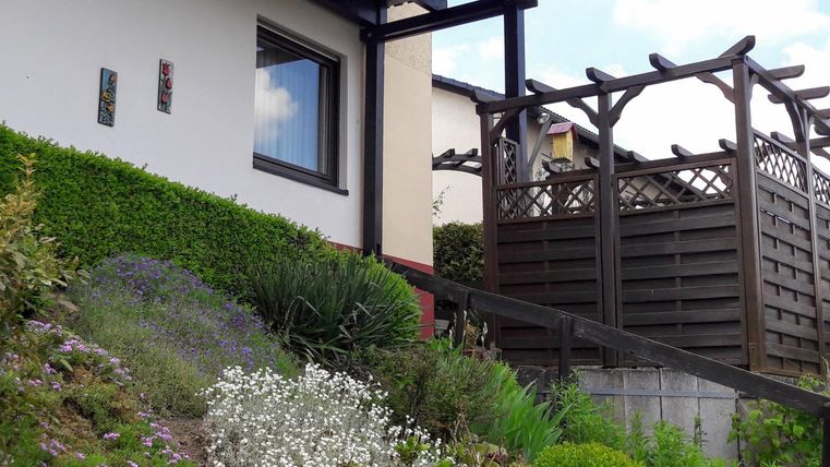 Een modern huis met een verzorgde tuin en kleurrijke bloemen. Op de achtergrond is een houten terras te zien.