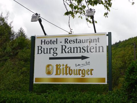 Ein Schild für das Hotel und Restaurant Burg Ramstein. Es zeigt die Richtung zur Burg und beinhaltet das Bitburger-Logo.