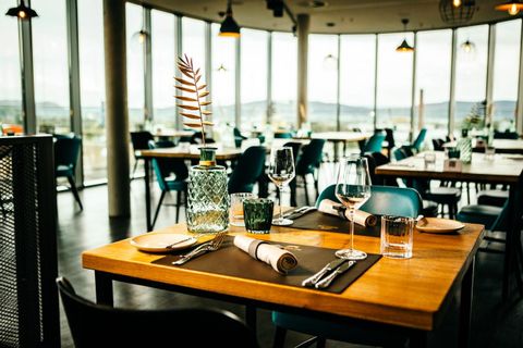 Ein elegantes Restaurant mit großen Fenstern und moderner Einrichtung. Der Tisch ist stilvoll gedeckt mit Gläsern und dekorativen Elementen.