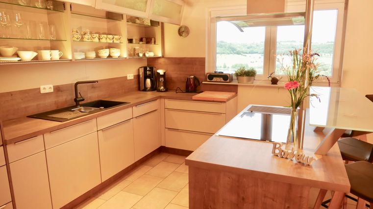 A modern kitchenette with bright cabinets and a cooking area. Large windows provide plenty of daylight and a view of the outdoors.