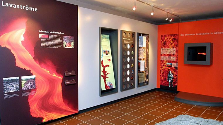 Ein modernes Ausstellungszimmer mit Informationen über Lavastrom. Verschiedene Informationswände und interaktive Elemente sind sichtbar.