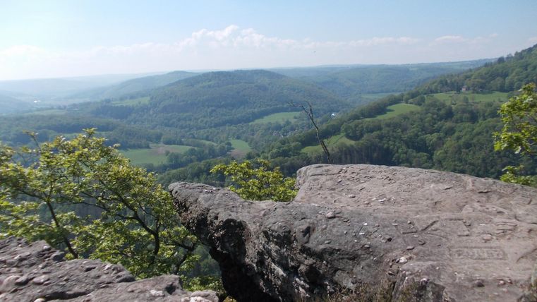 An impressive view from a rock overlooking green hills and gentle landscapes. The sky is clear and brilliantly blue.