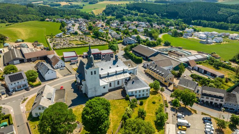 Een schilderachtig uitzicht op een dorp met een kerk in het midden. Omgeven door groene velden en woongebouwen straalt het landschap rust uit.