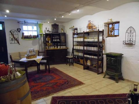 A cozy room with shelves full of bottles and a table. The floor is tiled, and there is a rustic atmosphere with decorative elements.