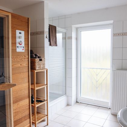 Ein modernes Badezimmer mit einer Sauna und einer Dusche. Große Fenster sorgen für viel Tageslicht.