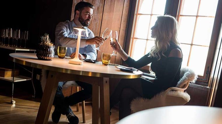 Een romantisch diner bij kaarslicht. Een stel proost in een gezellige kamer met houten decor.
