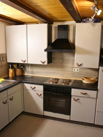A modern kitchen with white cabinets and a black stove. The wooden ceiling gives the kitchen a cozy atmosphere.
