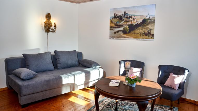 A cozy living space with a gray sofa and two blue chairs. On the table, there is a small flower vase and a picture hangs on the wall.