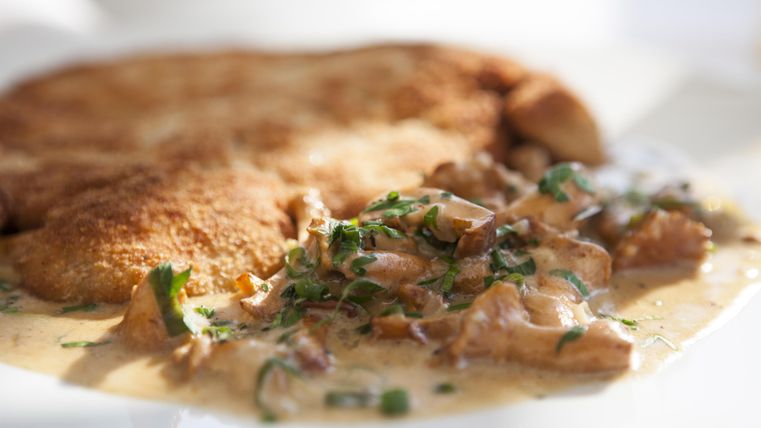 Een heerlijk gerecht met een knapperige korst en een romige champignonsaus. Het eten is gegarneerd met verse kruiden.