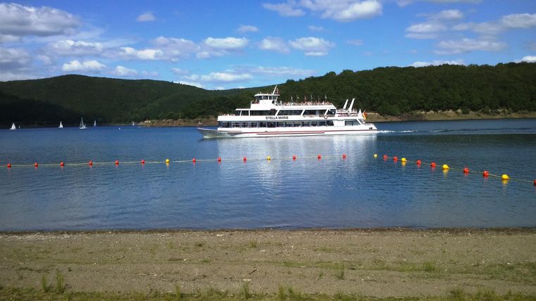 Ein schönes Gewässer mit einem Boot, das sanft fährt. Im Hintergrund sind Hügel und ein blauer Himmel mit Wolken sichtbar.