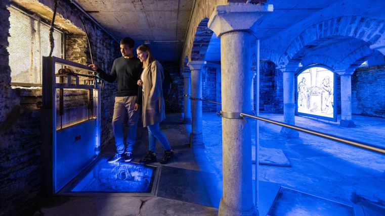 Een moderne kelder met blauwe verlichting. Twee personen verkennen de ruimte die is ingericht met pilaren en ramen.