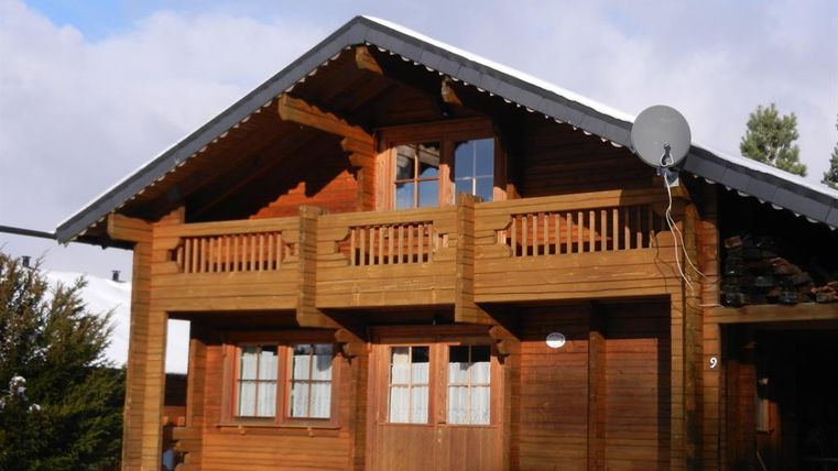 Ein gemütliches Holzhaus im Schnee mit einem Balkon und großen Fenstern. Der Himmel ist teilweise bewölkt.