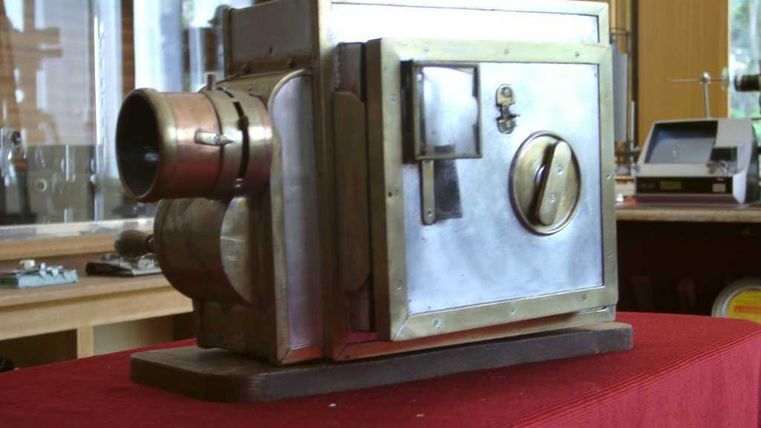 Eine alte Kamera aus Metall mit einem eleganten Design. Sie steht auf einem roten Tisch in einem Ausstellungsraum.