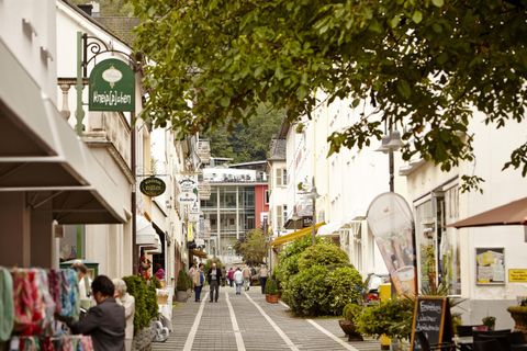 Eine malerische Straße mit Geschäften und Bäumen. Menschen schlendern entspannt entlang der Fußgängerzone.