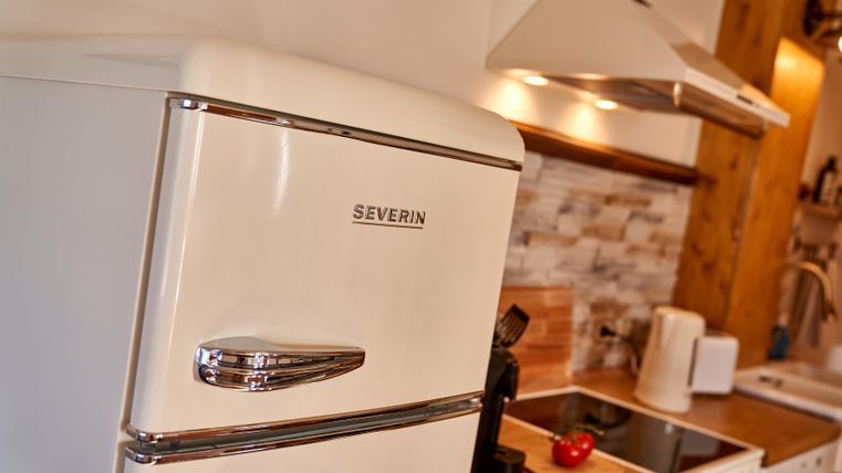 A modern kitchen with a classic white refrigerator. In the background, there are wooden shelves and kitchen appliances.