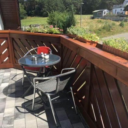 Een gezellige balkon met een ronde tafel en twee stoelen. Op de achtergrond zijn groene weilanden en bomen te zien.