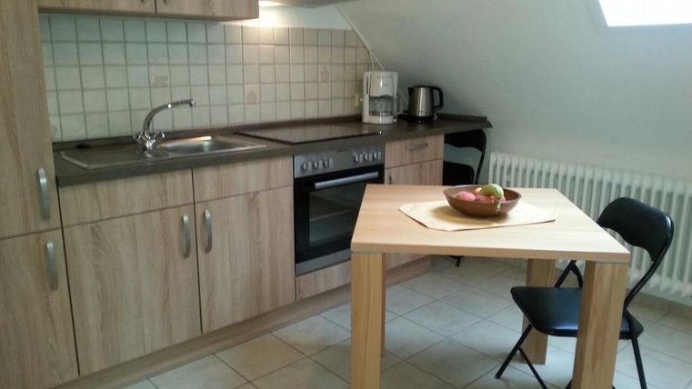 Eine moderne Küche mit Holzschränken und einer Arbeitsfläche. Auf dem Tisch liegen einige Äpfel und ein Stuhl steht bereit.