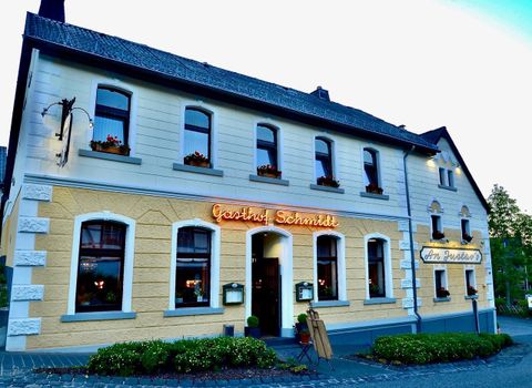 Een uitnodigende herberg met het opschrift "Gasthof Schmidt" op de gevel. De gevel is in vriendelijke kleuren gehouden en versierd met bloemen.