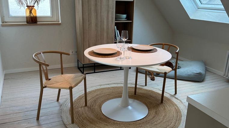 Een gezellige eetruimte met een ronde tafel en twee stoelen. Het raam zorgt voor veel daglicht en de decoratie is minimalistisch.
