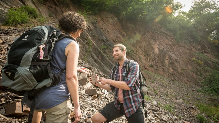 Zwei Personen bei einer geologischen Exkursion, eine zeigt auf einen Stein.