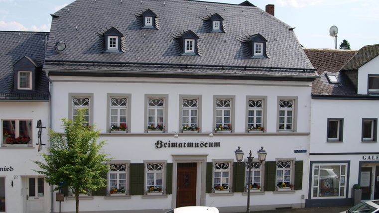Ein historisches Gebäude mit der Aufschrift "Heimatmuseum". Es hat eine schöne Fassade mit ansprechenden Fenstern und ist von Bäumen umgeben.