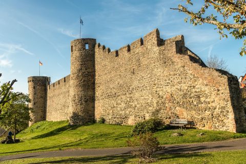 Eine alte Burgmauer mit Türmen und grünem Rasen. Der Himmel ist blau und es ist sonnig.