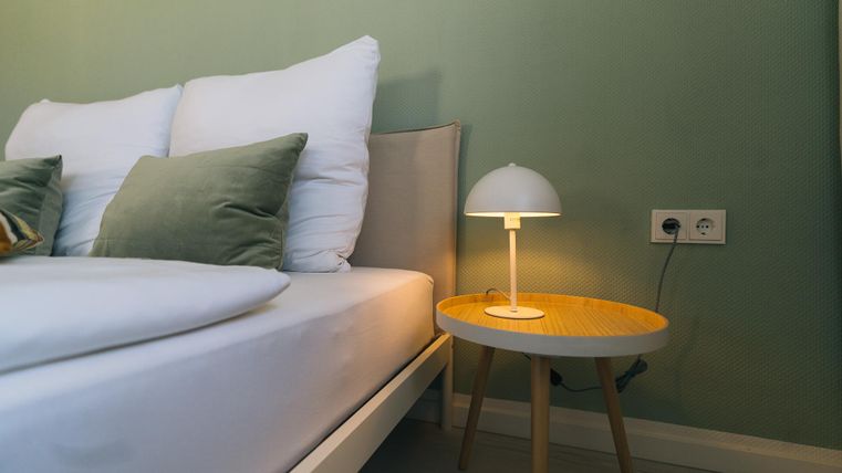 Een moderne slaapkamer met een wit bed en gezellige kussens. Op het nachtkastje staat een stijlvolle lamp met warm licht.