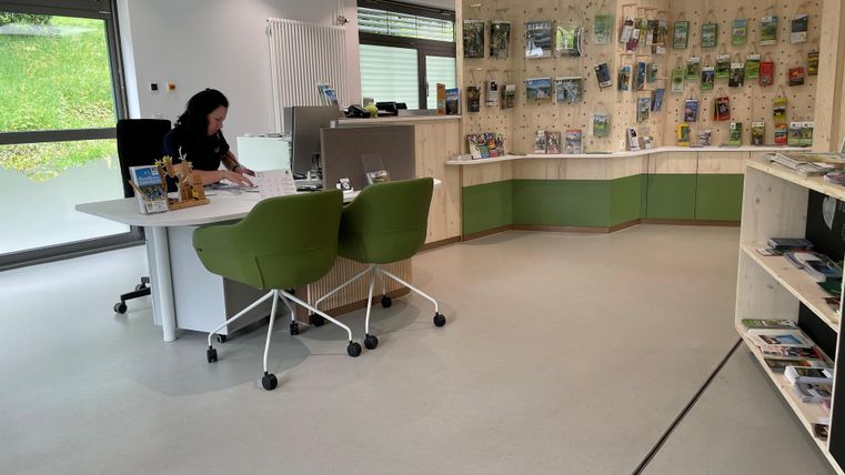 Een modern kantoor met een bureau en twee groene stoelen. Aan de muur zijn informatiematerialen en brochures tentoongesteld.