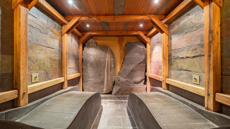 Een ontspannen wellnessruimte met twee loungestoelen van steen. De muren zijn gemaakt van natuurlijk gesteente en hout, wat een gezellige sfeer creëert.