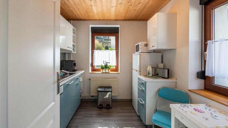 A modern kitchen with a wooden ceiling and bright walls.
On the table lies a colorful tablecloth and a chair is placed in the corner.