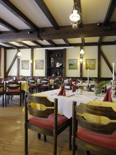 Ein gemütliches Restaurant mit Holzbalkendecke und eleganten Tischdecken. Die Tische sind für Gäste hergerichtet, mit Kerzen und Dekoration.