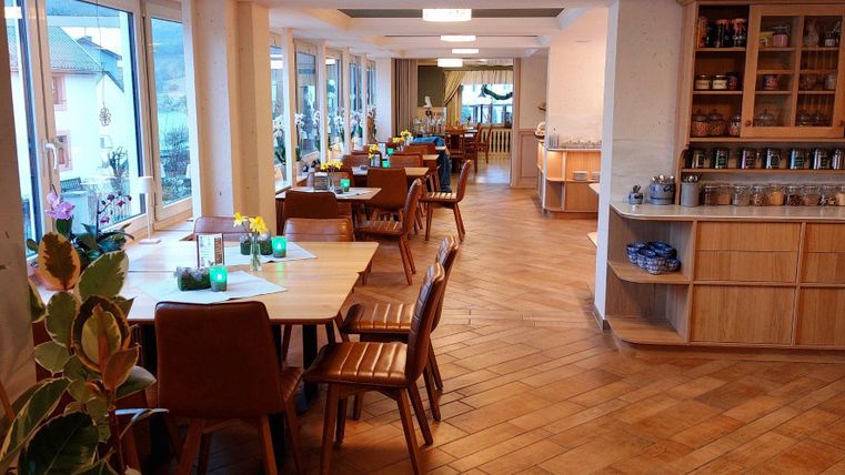 Ein modernes Restaurant mit Holzböden und großen Fenstern. Tische sind gemütlich gedeckt und einladend dekoriert.