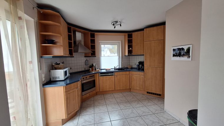 Eine moderne Küche mit Holzschränken und einem hellen Fußboden. Das Fenster sorgt für viel Tageslicht.