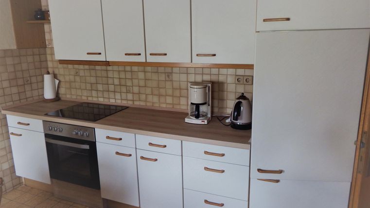 A modern kitchen with white cabinets and a dark countertop. There is a stove, a coffee machine, and an elegant kettle.