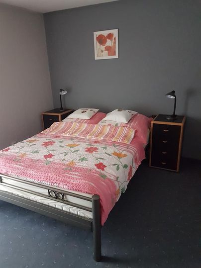 Ein Schlafzimmer mit einem Bett und bunten Bettwaren. An den Wänden befinden sich zwei Nachttische mit Lampen und ein Bild über dem Bett.