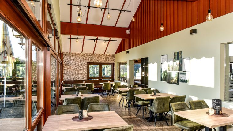 Ein gemütliches Restaurant mit großen Fenstern und Holzverkleidung. Die Tische sind in einem modernen Stil mit bequemen Stühlen eingerichtet.