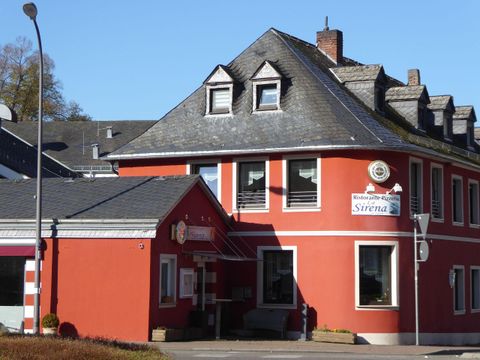 Ein rotes Gebäude mit einem interessanten Dach und Fenstern. An der Wand ist ein Schild mit der Aufschrift „Sirena“.