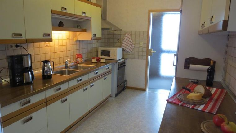 A modern kitchen with bright cabinets and a wooden countertop. On the work surface, there are apples and a plate with bread.