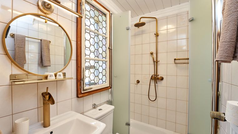 A modern bathroom with a shower and a white bathtub. It features elegant gold fixtures and a large, round mirror.