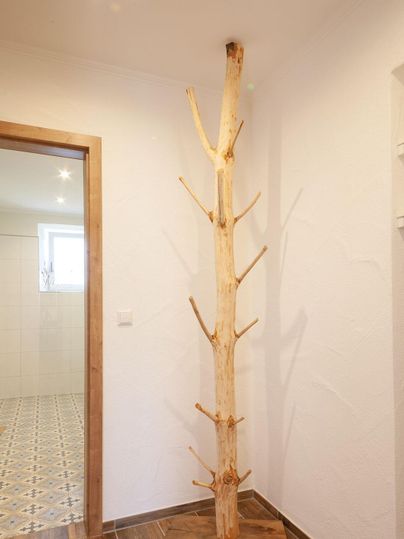 Ein natürlicher Holzbaum steht in einer modernen Ecke. Der Baum hat mehrere Äste und fügt sich harmonisch in die Umgebung ein.