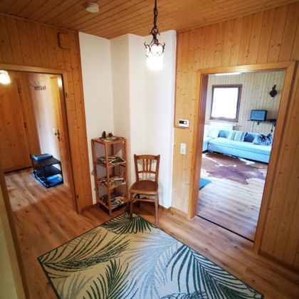 Een uitnodigende gang met houten panelen, een lamp en een stoel. Op de vloer ligt een tapijt met palmmotief.