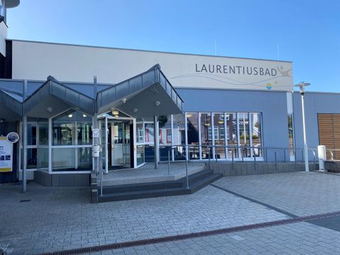 Das Laurentiusbad ist ein modernes Schwimmbad mit einer einladenden Eingangsfront. Es befindet sich in einem gepflegten Umfeld unter klarem Himmel.