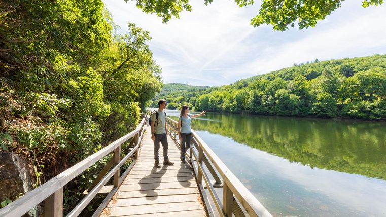 Een wandelpad langs een rustige rivier omringd door weelderig groen. Twee personen verkennen de natuur en genieten van het uitzicht.